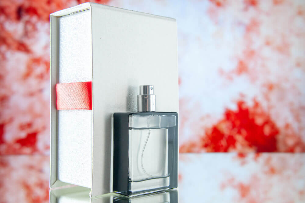 Caixa de perfume e vidro de perfume do lado com fundo de flores vermelhas